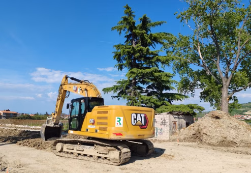 Excavator working at a construction site with trees and blue sky in the background