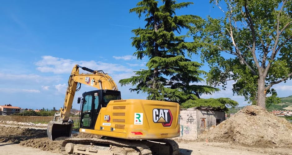 Excavator working at a construction site with trees and blue sky in the background